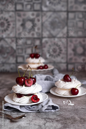 Mini Pavlova desserts with whipped cream and fresh cherries on a gray background. Meringue with berries. Light summer desserts.