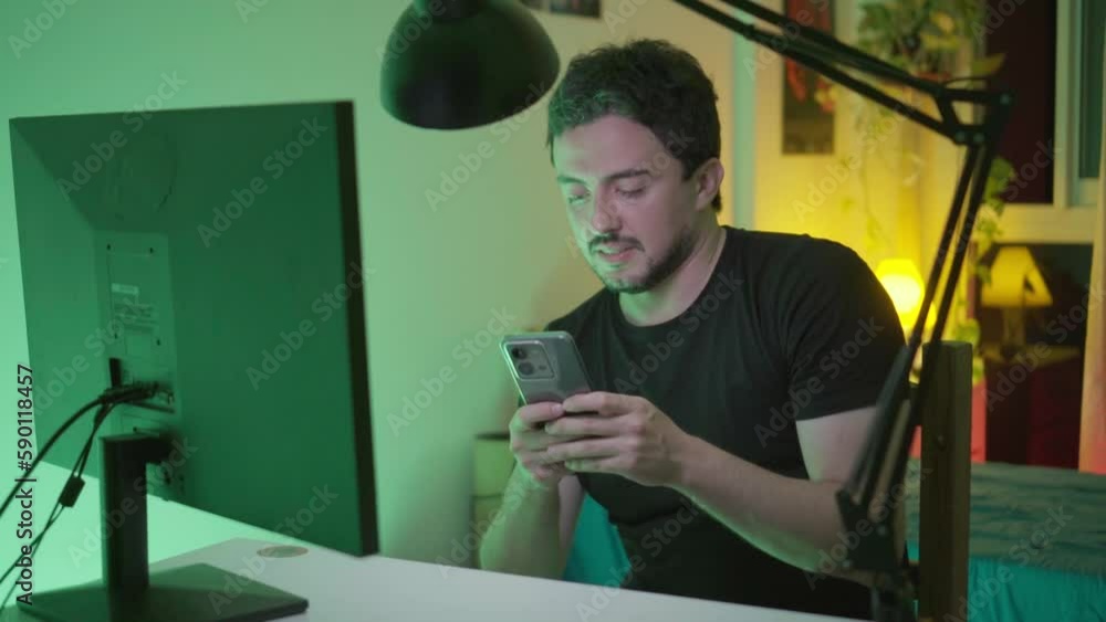 Young latin man texting on his cell phone while ignoring the video call on his desktop computer. Copy space. Young latin man texting on his cell phone while ignoring the video call on his desktop computer. Copy space.