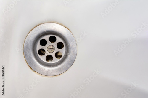 An old rusty bathtub with a metal drain hole. Dirty cracked unclean surface of the bath or sink with rust stain and lime deposits, close-up. Corrosion, unsanitary concept