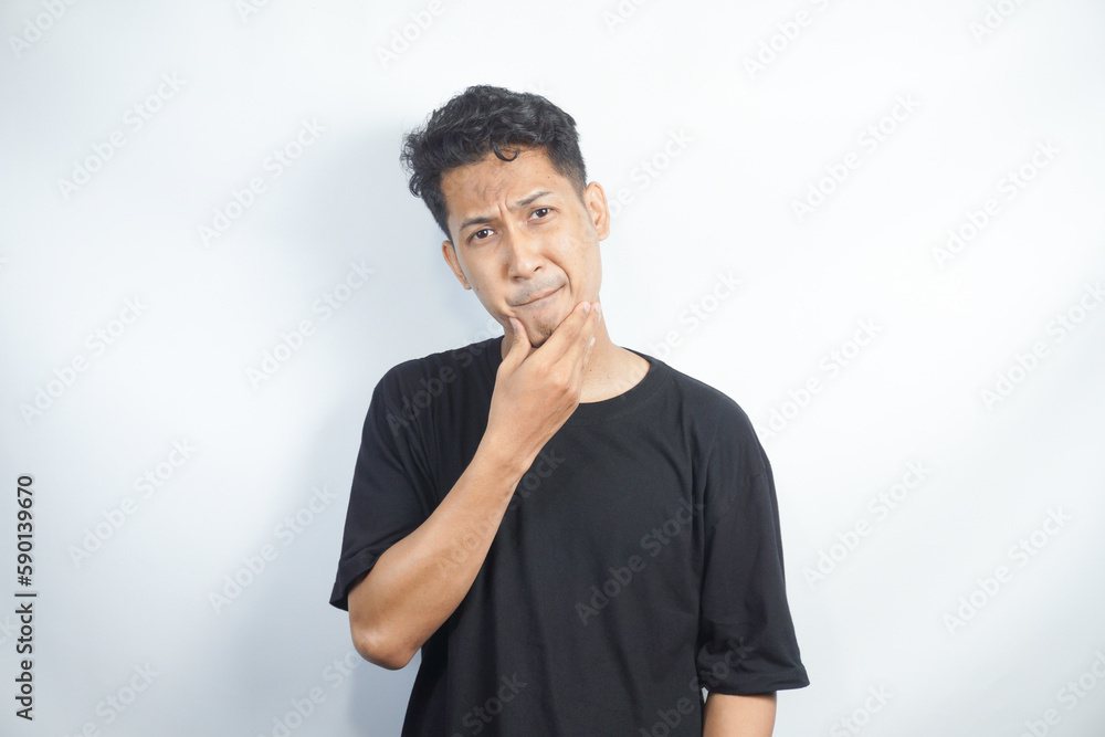 Portrait of unhappy determined Asian male  touching chin while thinking and looking with serious and worried look at camera, standing against white background.