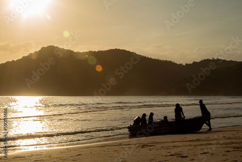 pôr do sol em linda praia com montanhas ao fundo e silhueta de barco chegando na praia com pescadores. photo