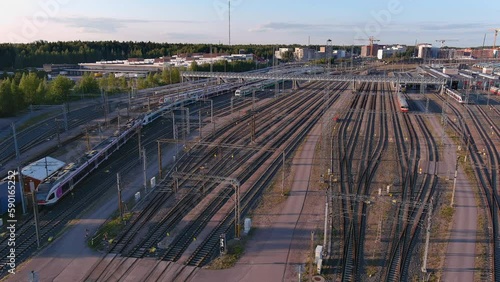 Helsinki.Finland-August 30.2021: Idyllic aerial shot of a train slowly driving through a railway station. Scandinavian architecture. Blue sky in the background. Drone moving sideways and forward. photo