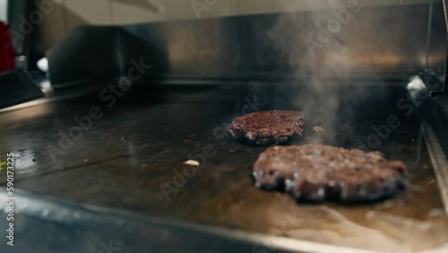 Professional restaurant kitchen close-up chef flips delicious juicy patties on grill with spatula for smash burger