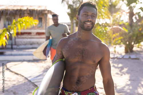 Portrait of happy african american man holding surfboard and smiling at beach