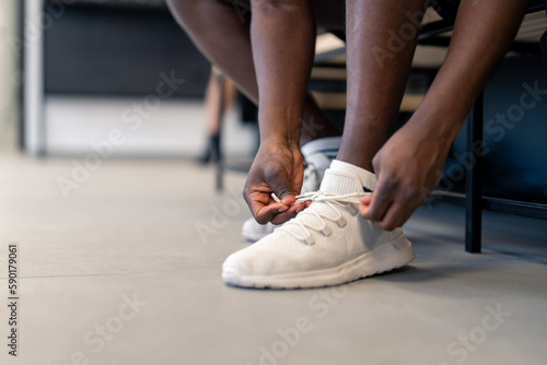Cropped shot of unrecognizable sportsman fitness coach or gym client sitting on bench tying his shoelaces in locker room at gym getting ready to exercise workout and keep his body fit and healthy.