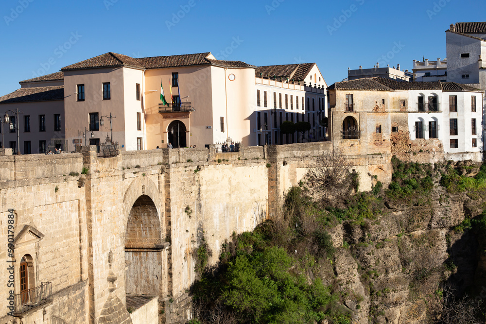 Ronda, Andalusia, Spain - March 15, 2023: Landscape of old white buildings and a bridge between the rocks of the gorge on a sunny day. Landmark of the city.