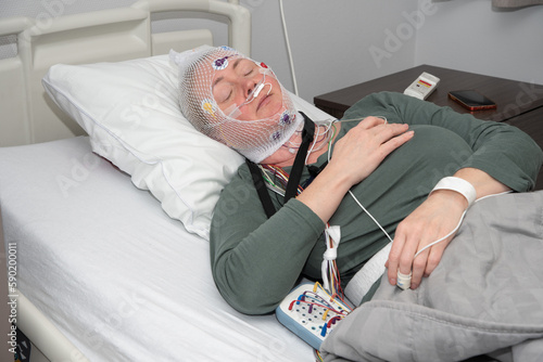 Middle aged woman measuring brain waves, examining polysomnography in sleep lab