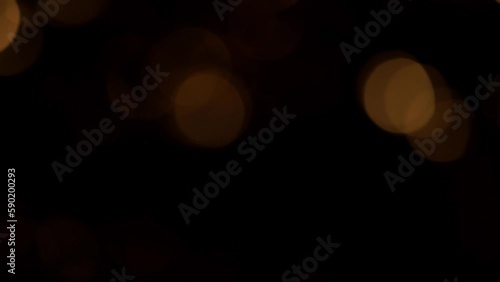 Slow movement of Golden Sepia Bokeh on a Black Background. Beautiful luminous overflow transition of defocused glitter circles. Abstract moving background of glowing bokeh lights.