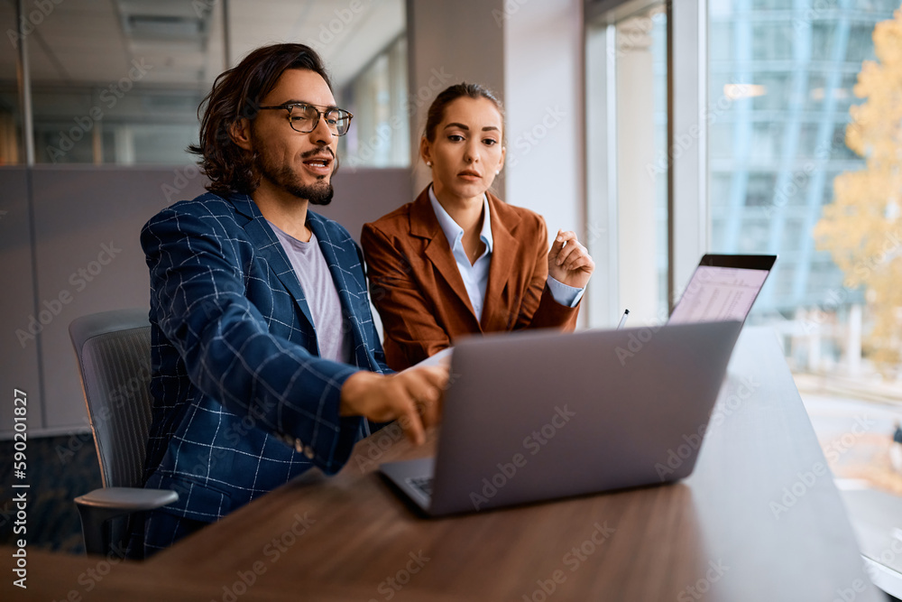 Young businessman talks to female colleague while working on computer in office. Young businessman talks to female colleague while working on computer in office.