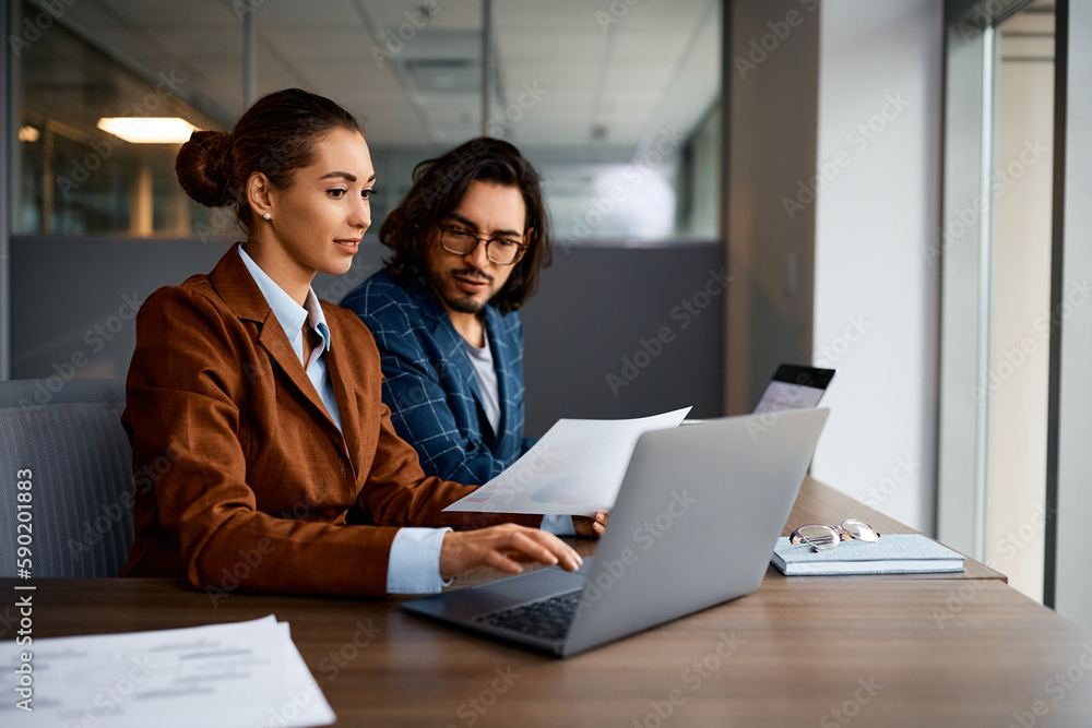 Young businesswoman and her colleague using laptop while analyzing reports in office. Young businesswoman and her colleague using laptop while analyzing reports in office.