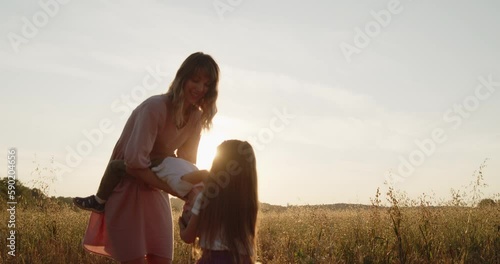 Happy young mother have fun with her little children spending time together in a wheat field at sunset. Mom playing with her son holding him with hands laughing during golden hour. photo