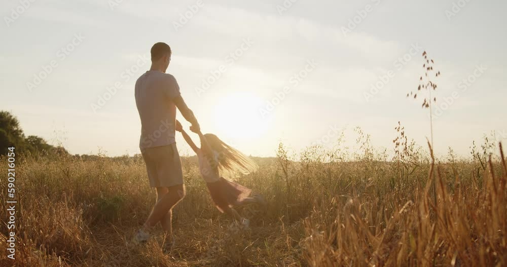 Happy young father have fun with his little daughter spending time together in a wheat field at sunset. Dad spinning his daughter holding hands laughing during golden hour. Happy young father have fun with his little daughter spending time together in a wheat field at sunset. Dad spinning his daughter holding hands laughing during golden hour.