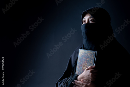 Portrait Asian Muslim woman standing and reading the Quran and appreciating and faith The Holy Al Quran with written Arabic calligraphy meaning of Al Quran, Arabic word translation: The Holy Al Quran.