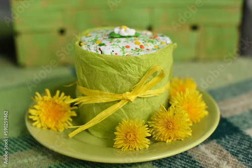 Easter Cake decorated with sugar glaze and yellow flowers are on green checkered blanket. Picnic outdoors. Top view