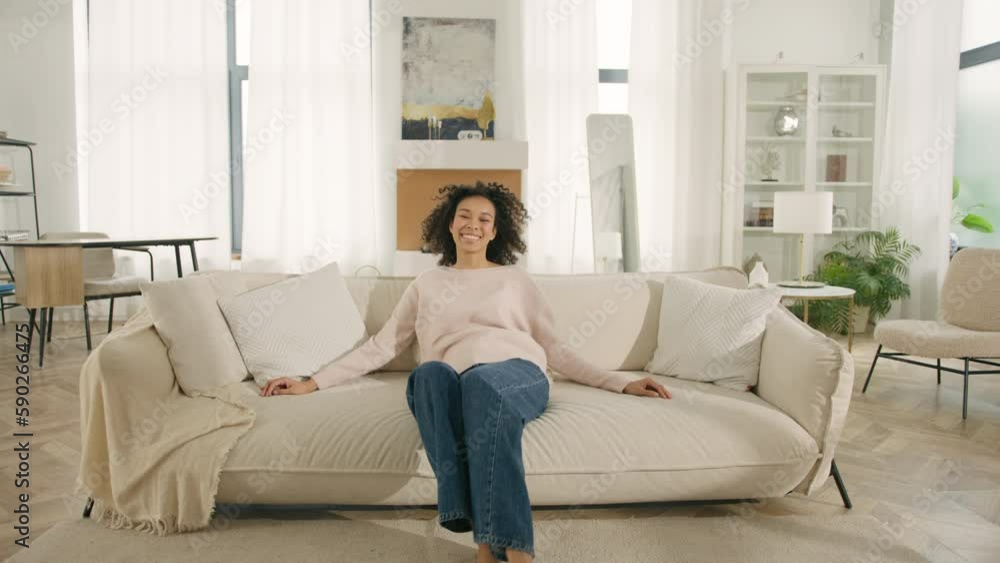 Afro girl laughing, enjoying rest on cozy sofa, feeling overjoyed, celebrating move in day to home, rented flat. Design interior furniture. Happy African American woman jumping on modern soft couch 4K Afro girl laughing, enjoying rest on cozy sofa, feeling overjoyed, celebrating move in day to home, rented flat. Design interior furniture. Happy African American woman jumping on modern soft couch 4K