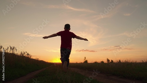 Child runs with his arms raised like wings of an airplane, childhood dream travel, nature. Child pilot runs through field of sunflowers, kid dreams, airplane pilot. Silhouette of boy running at sunset