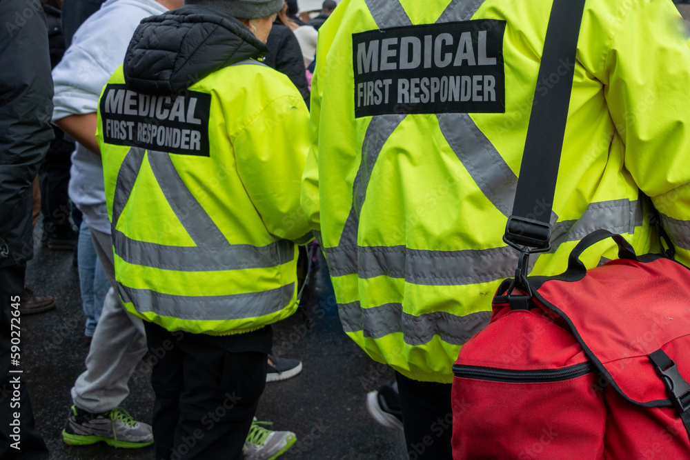 Medical first responders walk along a road wearing black wool stocking caps, and yellow