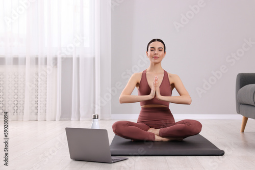 Woman in sportswear meditating near laptop at home, space for text