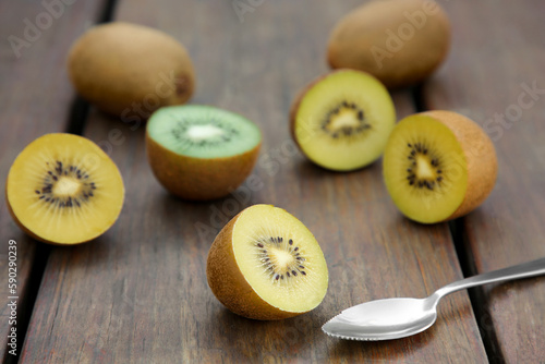 Spoon with many whole and cut fresh kiwis on wooden table