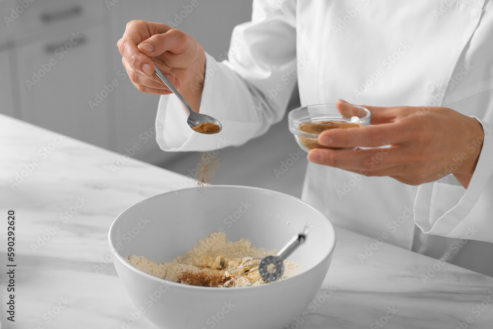 Professional chef adding cocoa powder into dough at white marble table indoors, closeup