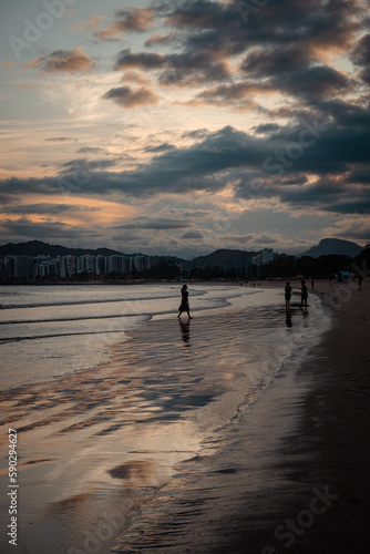 Sombra de mulher e pessoas na praia ao pôr-do-sol  com nuvens no céu 