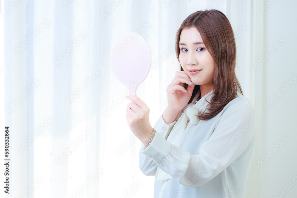 	手鏡を持ち頬に手を当てたカメラ目線の女性