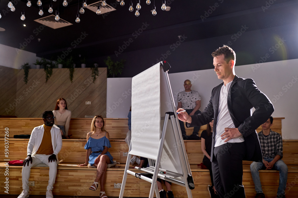 © Roman - Male speaker giving presentation to students in hall at university.conference hall. Participants sit listening while speaker is writing on board. Scientific, business event, training. Education © Roman - Male speaker giving presentation to students in hall at university.conference hall. Participants sit listening while speaker is writing on board. Scientific, business event, training. Education