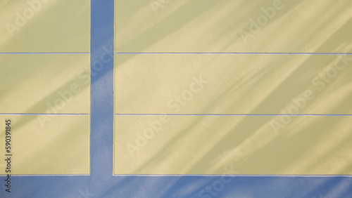 Sunlight and tree branches shadow on yellow concrete fence wall with blue lines stripes on surface