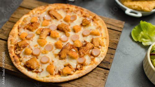 Top view shot of delicious tasty juicy sliced sausage cheesy pizza placed on wooden board around with other fast food crispy fried chicken, seasoning ingredients and fresh raw organic vegetables