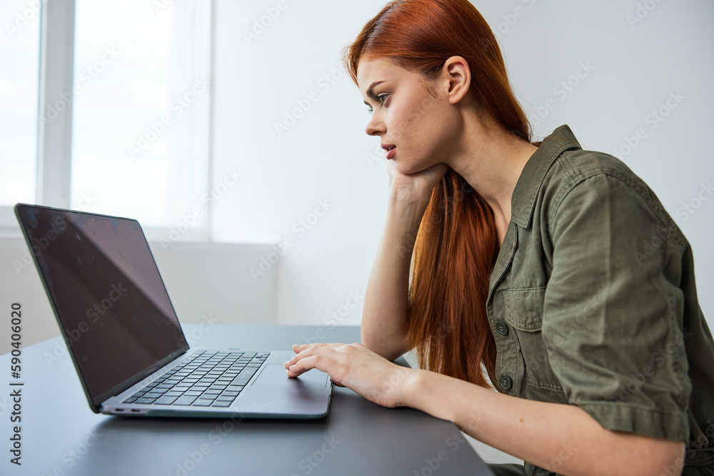 woman interested in work sits at a table and works in a laptop in a bright room woman interested in work sits at a table and works in a laptop in a bright room