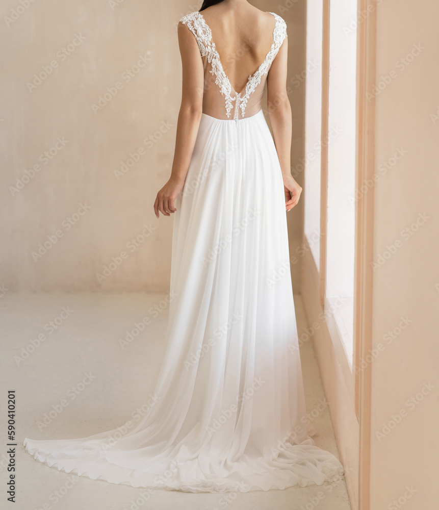 Back view of beautiful brunet model in the white wedding dress with the naked back. Gorgeous sleeveless wedding dress decorated with elegant lace and buttons Back view of beautiful brunet model in the white wedding dress with the naked back. Gorgeous sleeveless wedding dress decorated with elegant lace and buttons