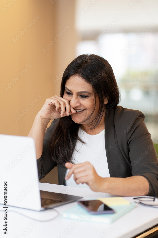 Smiling confident Indian woman using laptop computer having video call in office. Successful asian freelancer working online sitting at workplace. Modern technology, video conference concept Smiling confident Indian woman using laptop computer having video call in office. Successful asian freelancer working online sitting at workplace. Modern technology, video conference concept