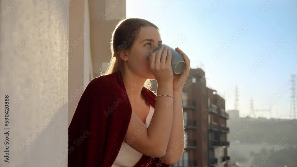 Smiling woman with plaid drinking coffee on balcony at morning. People relaxing, resting at home, beautiful cityscape Smiling woman with plaid drinking coffee on balcony at morning. People relaxing, resting at home, beautiful cityscape