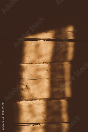 Warm orange uneven wooden log wall of rough texture with a sun light spot reflection from the window. Abstract background. Country style. Shadow. Natural old plank. Aged wall finish. Atmospheric