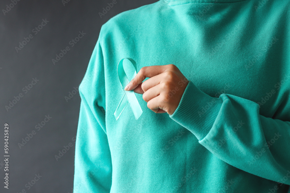 Woman hands wearing teal t-shirt holding teal awareness ribbon. Support cancer survivor. Ovarian Cancer month, cervical cancer day. Woman hands wearing teal t-shirt holding teal awareness ribbon. Support cancer survivor. Ovarian Cancer month, cervical cancer day.