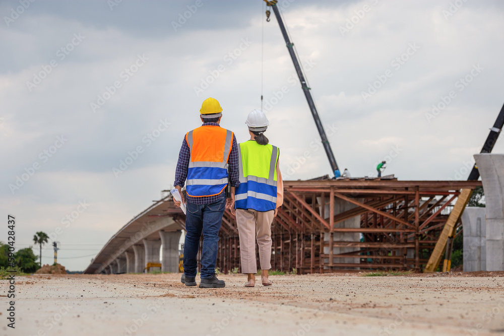 Fototapeta premium Female engineer and foreman worker checking project at building site, Engineer and builders in hardhats discussing on construction site, Teamwork concepts