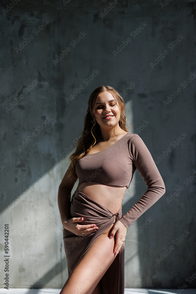 A happy young pregnant woman in a brown delicate suit is posing and stroking her belly. Pregnant pregnant woman. Happy pregnancy