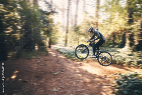 Cycling, jump and fast with man in nature for adventure, fitness and extreme sports. Workout, exercise and speed with male cyclist on bike in forest park for action, performance and training