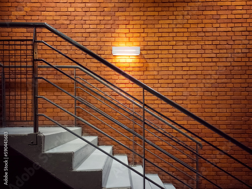 Side view of the stairs near the red brick wall. A light fixture on a brick wall illuminates the stairs