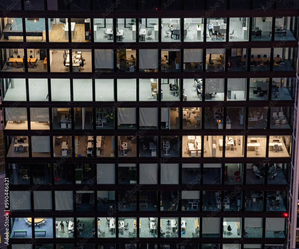 Façade of the glass high-rise with a different office on each floor with workers and light. Office life Façade of the glass high-rise with a different office on each floor with workers and light. Office life