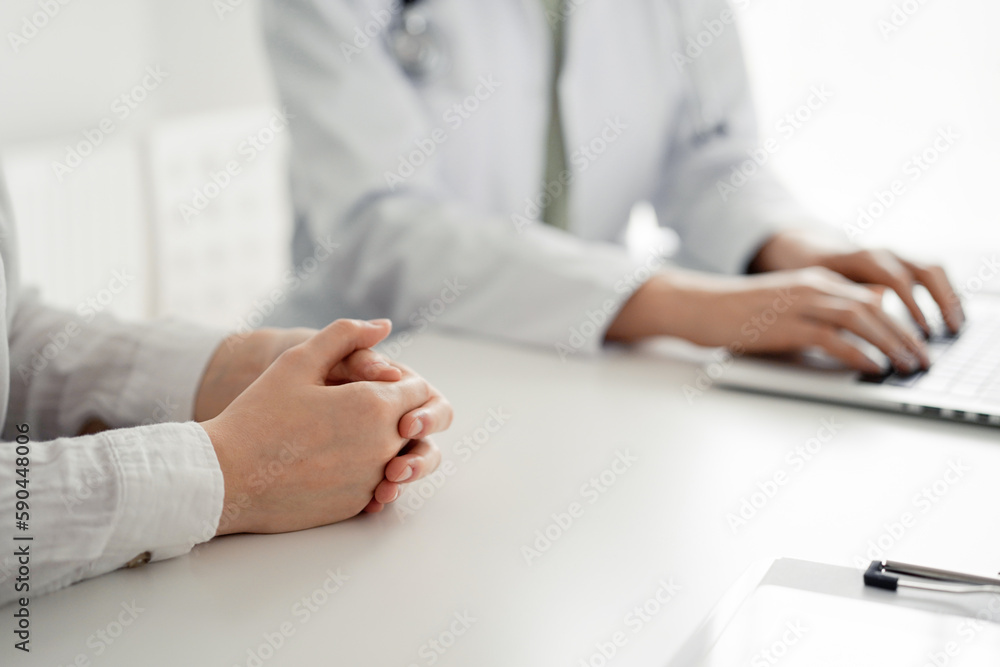 Doctor and patient discussing current health examination while sitting at the desk in clinic office. The focus is on female patient's hands, close up. Perfect medical service and medicine concept Doctor and patient discussing current health examination while sitting at the desk in clinic office. The focus is on female patient's hands, close up. Perfect medical service and medicine concept