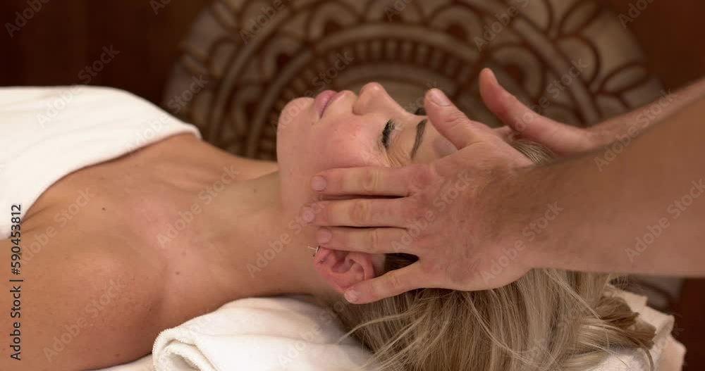 attractive female getting Ayurveda face massage by male hands of man in spa salon. Beautiful blonde lady enjoying day spa resort, lying down on table treatment procedure. facial procedure attractive female getting Ayurveda face massage by male hands of man in spa salon. Beautiful blonde lady enjoying day spa resort, lying down on table treatment procedure. facial procedure
