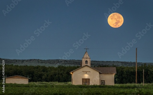 Mesmerizing shot of the full moonrise in a rural area and an old church in the foreground © Daniel Marquez/Wirestock Creators