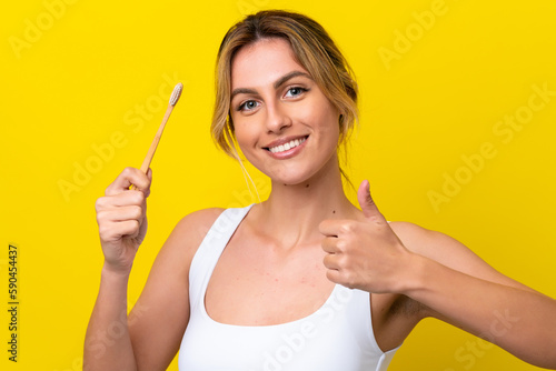 Young Uruguayan woman brushing teeth isolated on yellow background with thumbs up because something good has happened