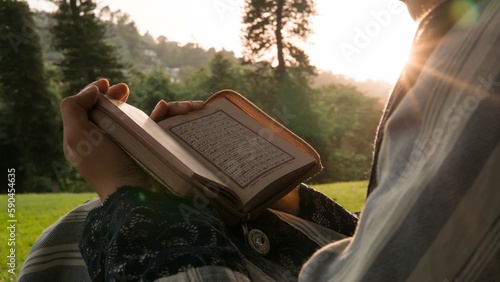 Woman reading holy book(Quran) in park at sunset, closeup. Religion concept