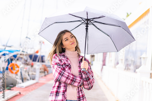 Young pretty Romanian woman holding an umbrella at outdoors with sad expression