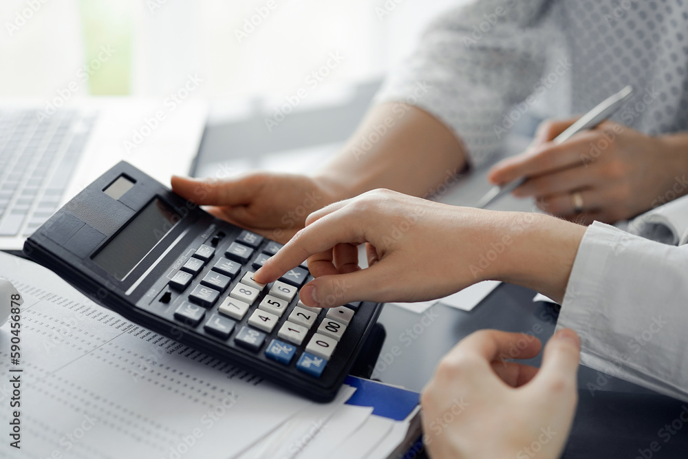 Woman accountant using a calculator and laptop computer while counting taxes for a client. Business audit and finance concepts Woman accountant using a calculator and laptop computer while counting taxes for a client. Business audit and finance concepts