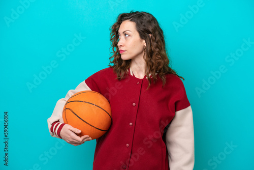 Young caucasian basketball player woman isolated on blue background looking to the side