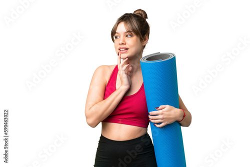 Young sport girl going to yoga classes while holding a mat over isolated chroma key background looking up while smiling