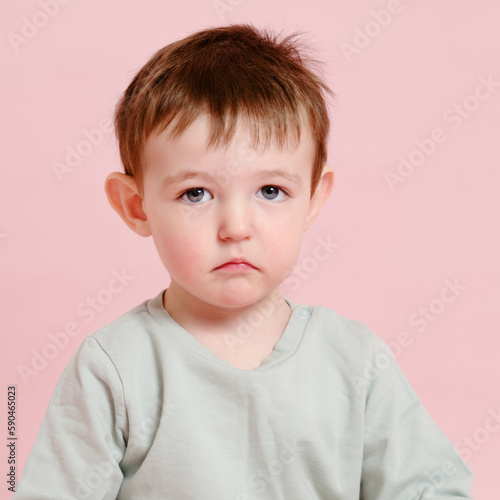 Sad toddler baby on studio pink background, copy space. Unhappy child boy face close-up. Kid age one year eight months